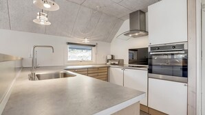 A modern kitchen with a stainless steel sink, a built-in oven, and pendant lights. - 3 bedroom beautiful home in Blåvand (Blåvand)