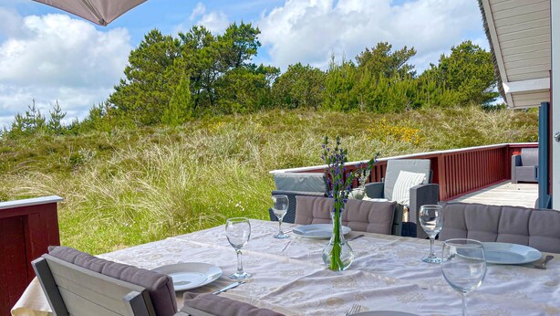 An outdoor dining area with a table set for two, surrounded by wicker furniture and a red deck. - 3 bedroom beautiful home in Blåvand (Blåvand)