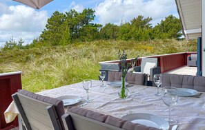 An outdoor dining area with a table set for two, surrounded by wicker furniture and a red deck.