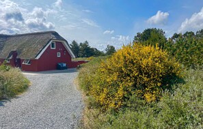A red barn with a gravel path leading to it, surrounded by greenery and yellow flowers.