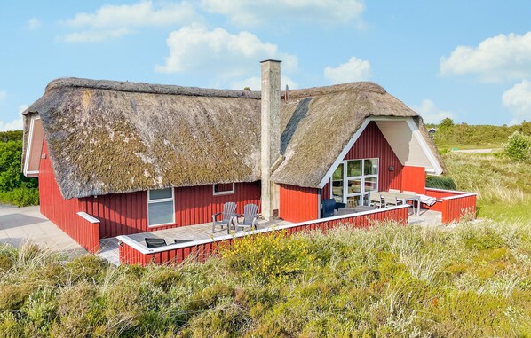 A red wooden house with a thatched roof and a small deck area with outdoor seating.