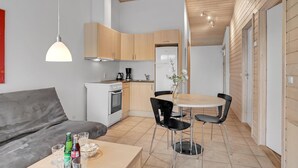 Een knus woongedeelte met een kitchenette, een eethoek met een ronde tafel en stoelen, en een grijze bank.