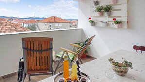 A balcony with a table set for a meal, a chair, a wooden barrel, and a view of houses in the background. - 2 bedroom lovely apartment in Zadar (Zadar)