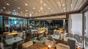A modern restaurant with wooden tables and chairs, large windows, and a ceiling with recessed lighting. - Cozy apartment in Imperia (Imperia)