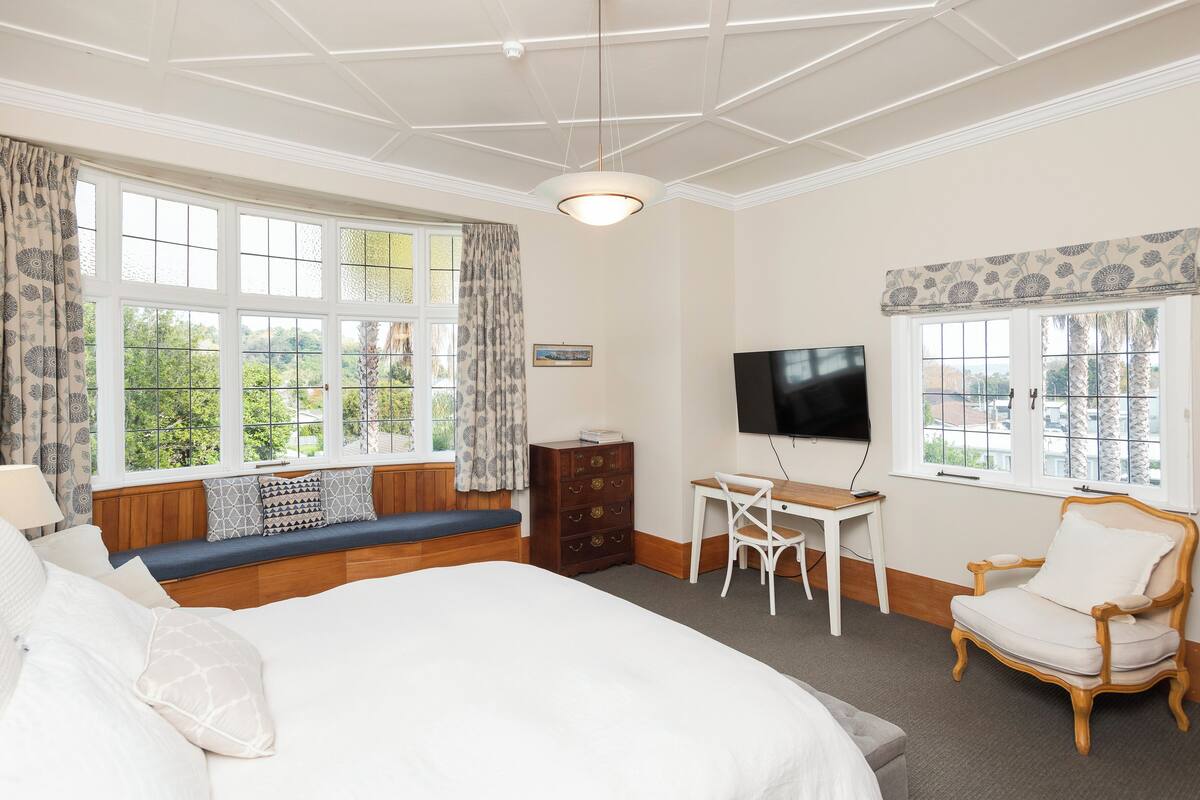 Un dormitorio con una cama grande, un escritorio con silla, televisión y una ventana con cortinas.