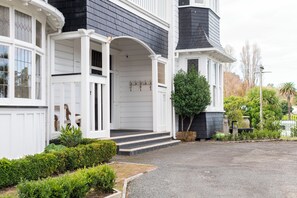 A two-story house with a white exterior and dark siding, featuring a front porch with steps and a small garden area. - Cedar House (Gisborne)