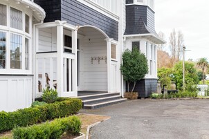 Una casa de dos pisos con fachada blanca y revestimiento oscuro, que cuenta con un porche con escalones y un pequeño jardín.