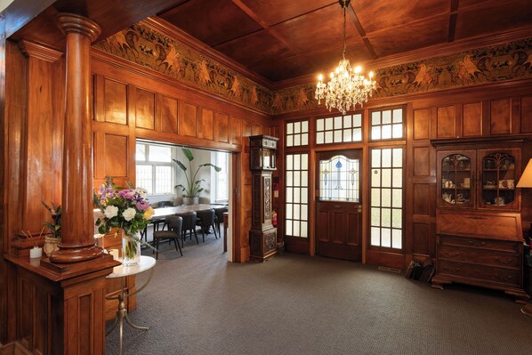 A spacious room with wooden paneling, a chandelier, a dining area with a table and chairs, and a large wooden cabinet. - Cedar House (Gisborne)