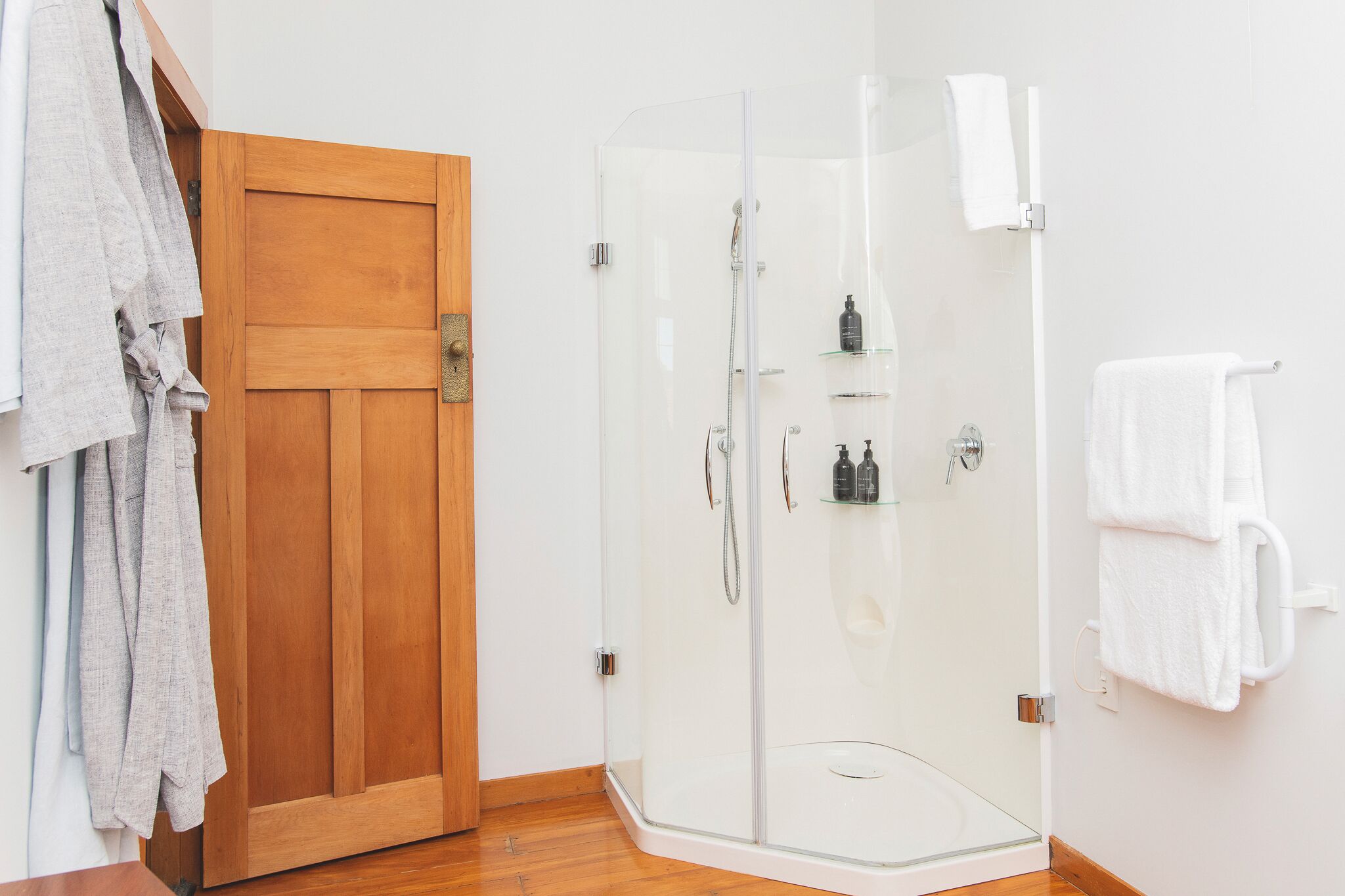A shower area with a glass door, a wooden door, and a towel rack with towels.