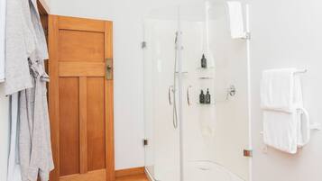 A shower area with a glass door, a wooden door, and a towel rack with towels.