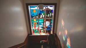 A staircase with a stained glass window featuring geometric patterns and a clock. - Cedar House (Gisborne)