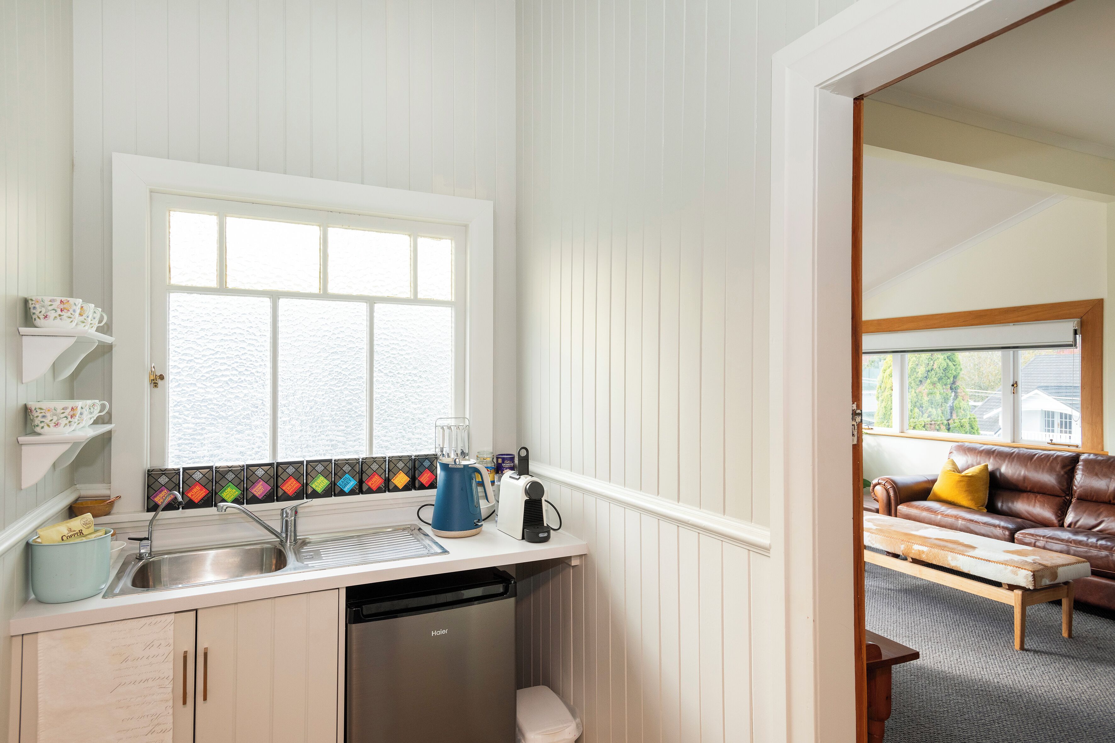 A kitchen with a built-in dishwasher, a window with a view, and a dining area with a brown leather couch.
