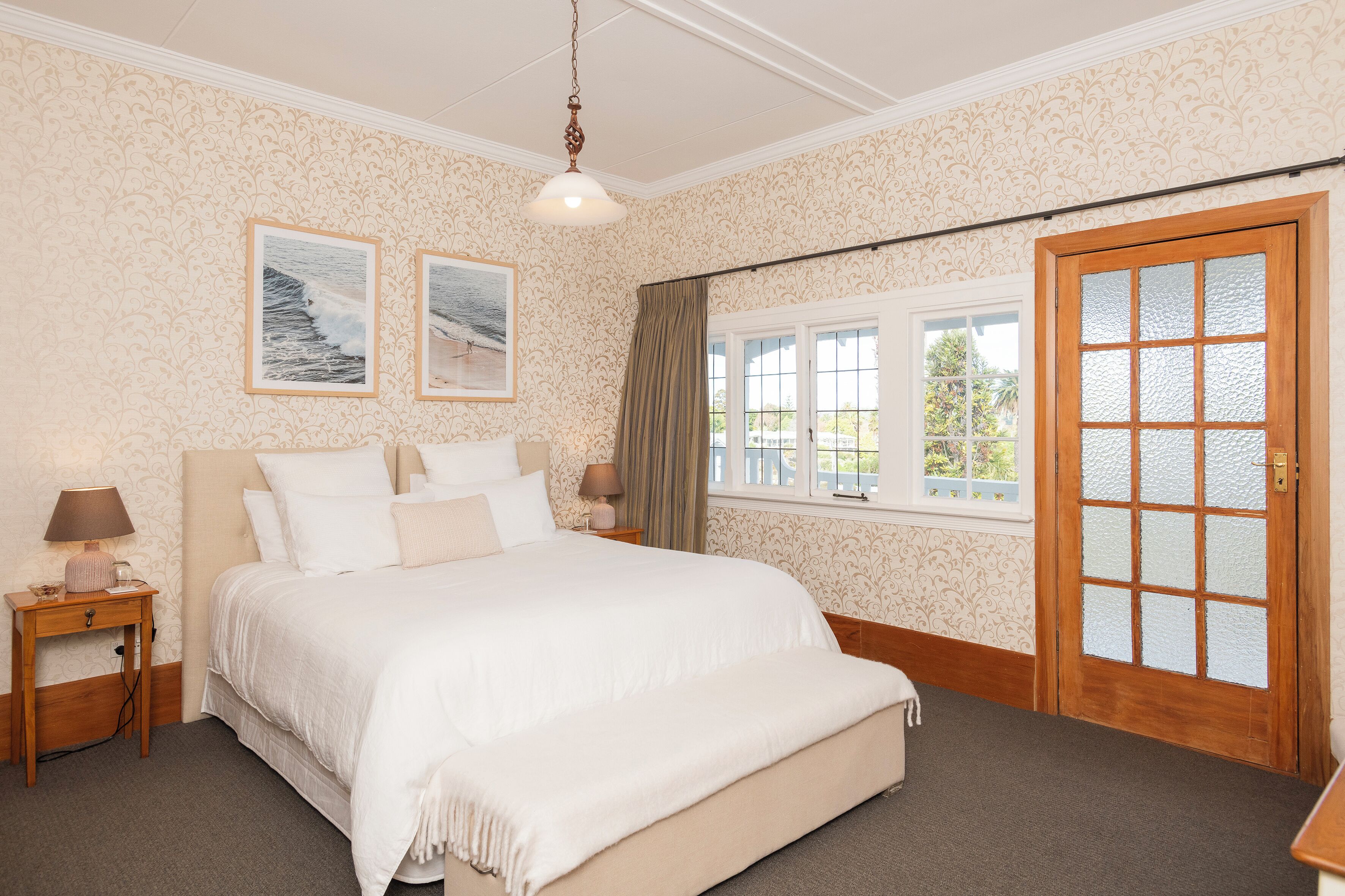 A bedroom with a large bed, two bedside tables, a window with a view, and a door with frosted glass panels.