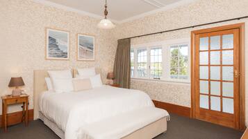 A bedroom with a large bed, two bedside tables, a window with a view, and a door with frosted glass panels.
