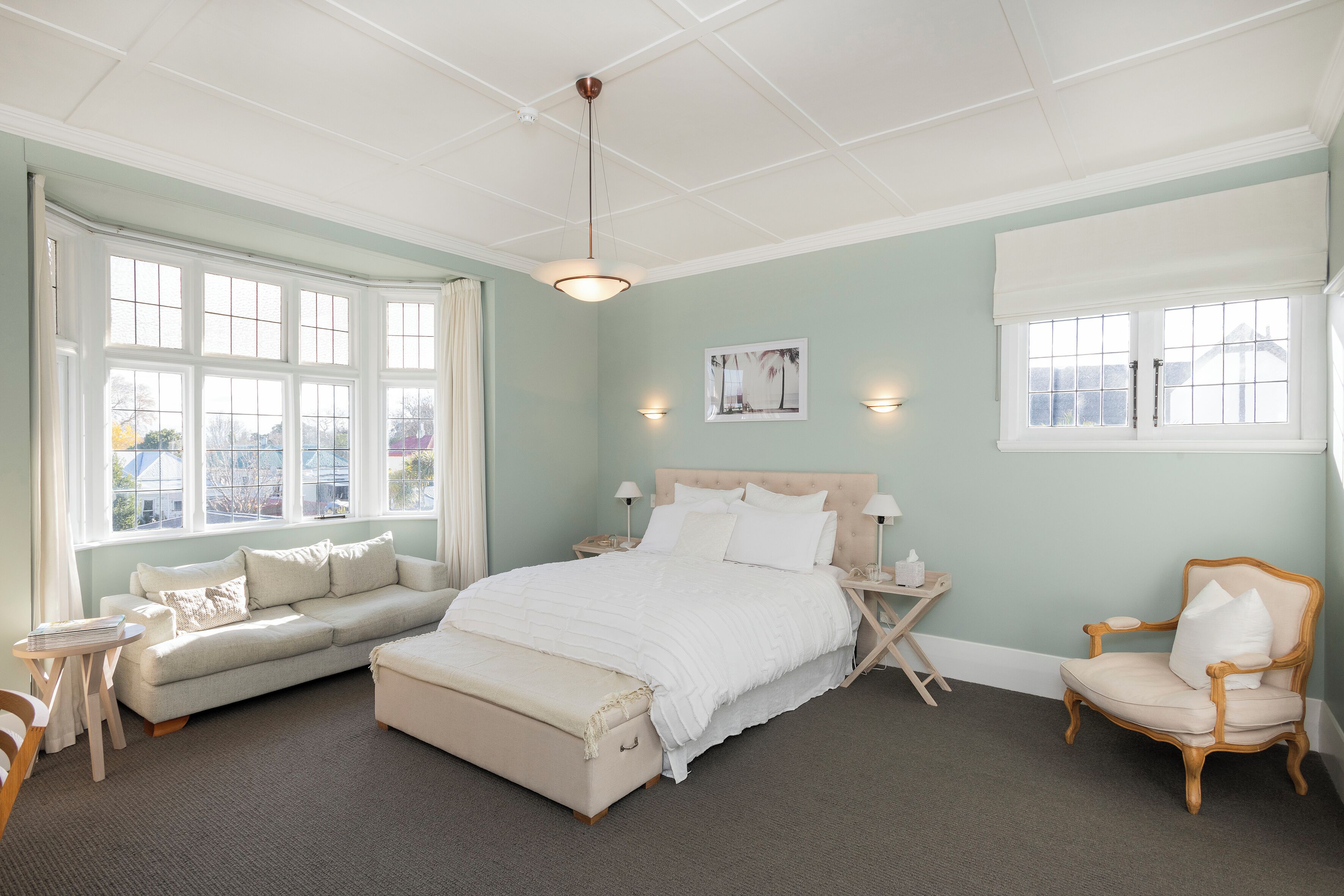 A bedroom with a large bed, a sitting area with a sofa and armchair, a small table, and a window with a view.