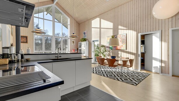 A modern kitchen with a large island, a dining area with a patterned rug, and a view of the outdoors through large windows.