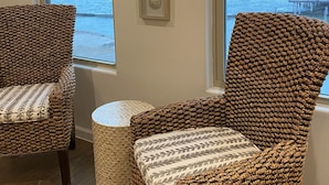 Ein Zimmer mit zwei Korbstühlen, einem kleinen runden Tisch und drei gerahmten Wanddekorationen.