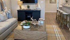 Ein modernes Wohnzimmer mit Flachbildfernseher, dunklem Holztisch und einem karierten Teppich.