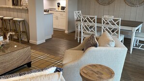 Ein modernes Wohnzimmer mit Sofa, Couchtisch und Essbereich mit weißem Stuhl und einer Pendelleuchte.