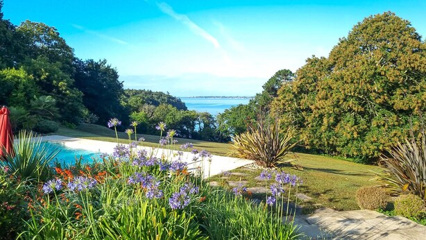 Ein Garten mit Pool, umgeben von üppiger Vegetation und Blick aufs Meer.