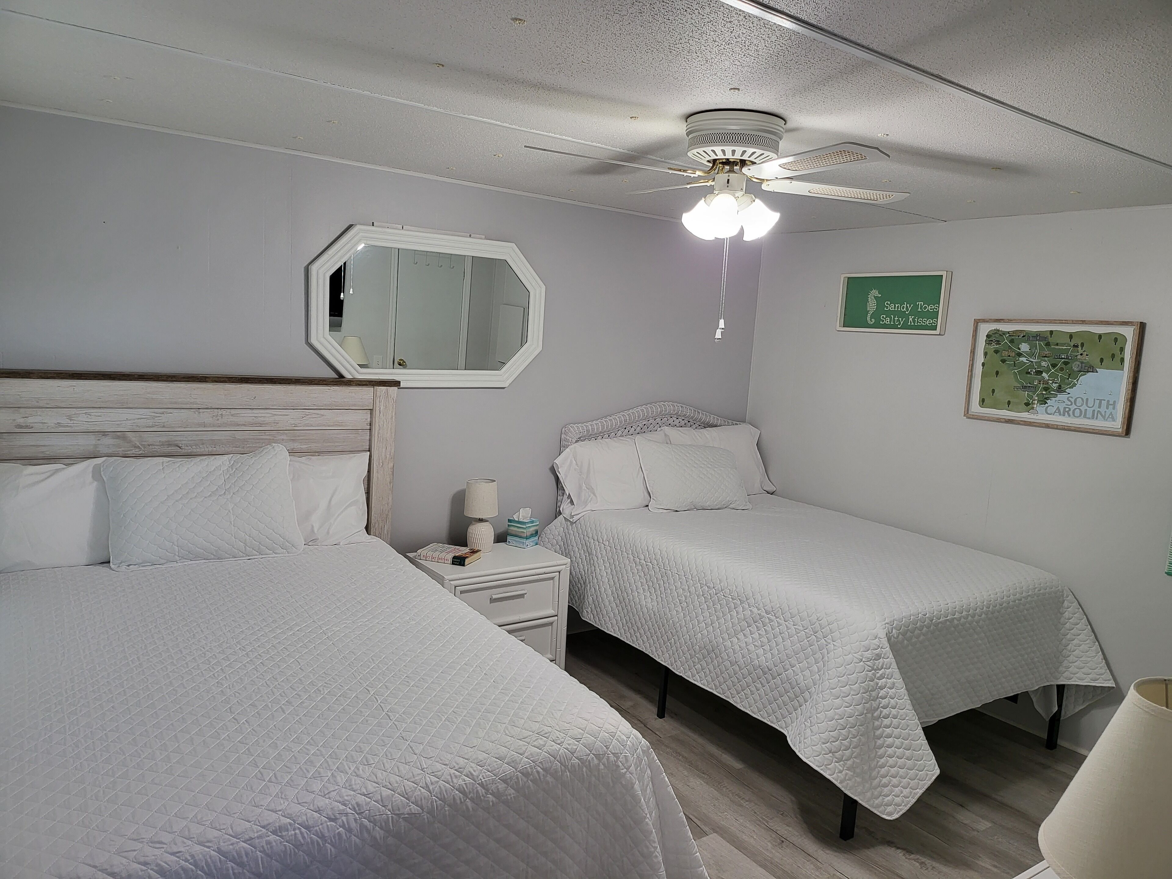 A bedroom with two beds, a nightstand, a mirror, a ceiling fan, and a map on the wall.
