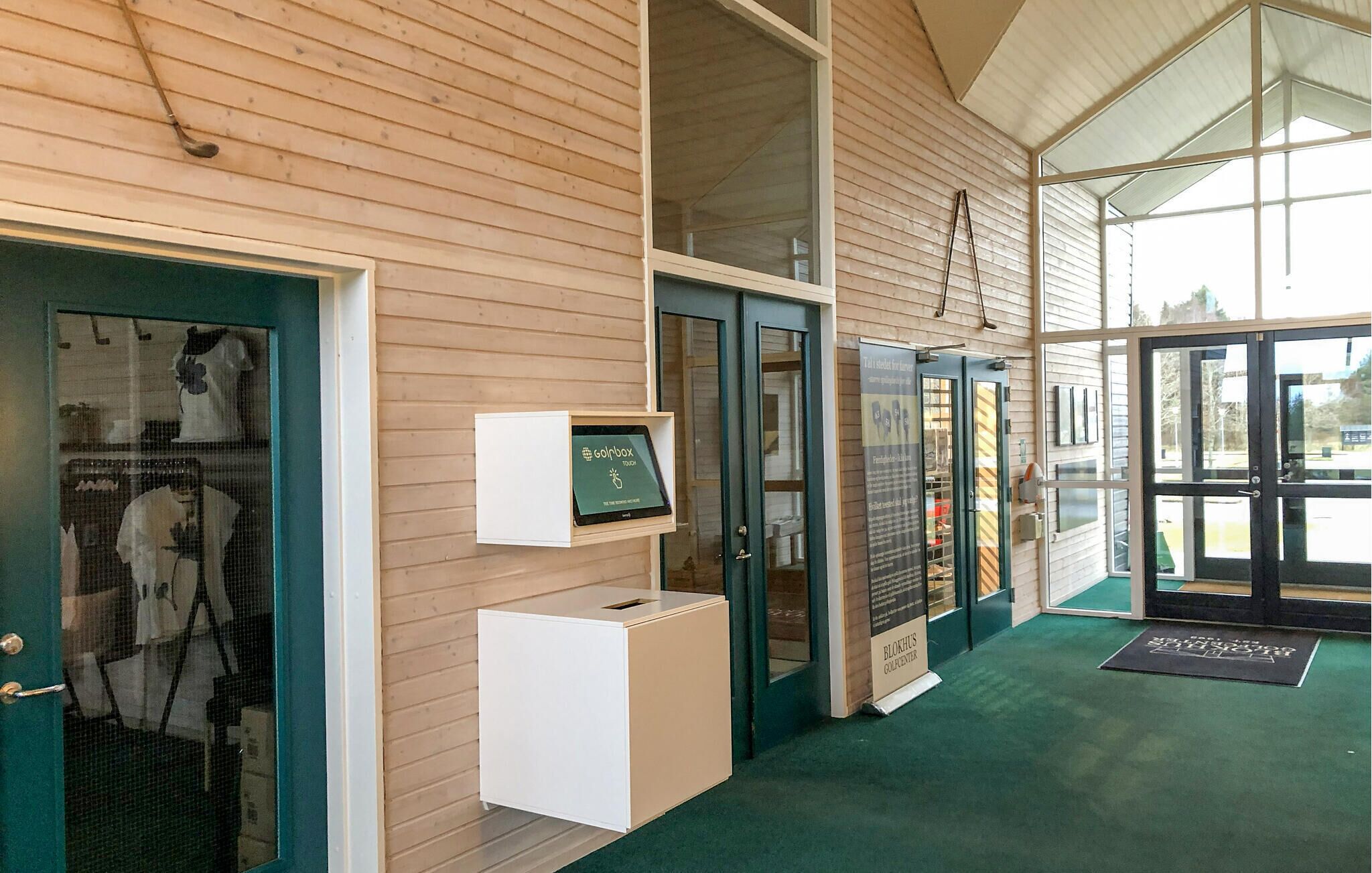 Un bâtiment moderne avec une façade en bois, un comptoir d’accueil et une grande porte vitrée.
