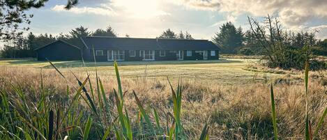 A two-story building with a flat roof, large windows, and a grassy field in the foreground.