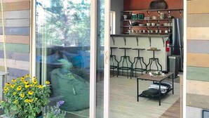 A modern interior with a glass door entrance, a seating area with tables and chairs, and a kitchen visible through the door.