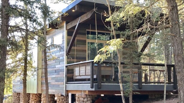 A cabin with a stone foundation, large windows, and a balcony with outdoor seating.