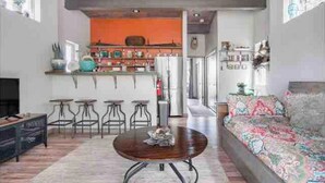 A modern living room with a wooden coffee table, a sofa, and a kitchen area with a bar counter and stools.