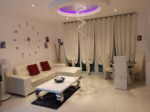 Un salon moderne avec un canapé blanc, des coussins rouges, une table basse blanche et un coin repas avec des chaises en osier.