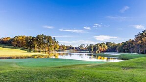 A golf course with a pond, trees, and a clear sky.