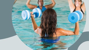A person in a swimming pool holding blue dumbbells.