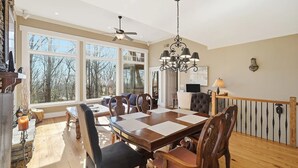 A dining room with a large table, chairs, a chandelier, and a view through large windows.