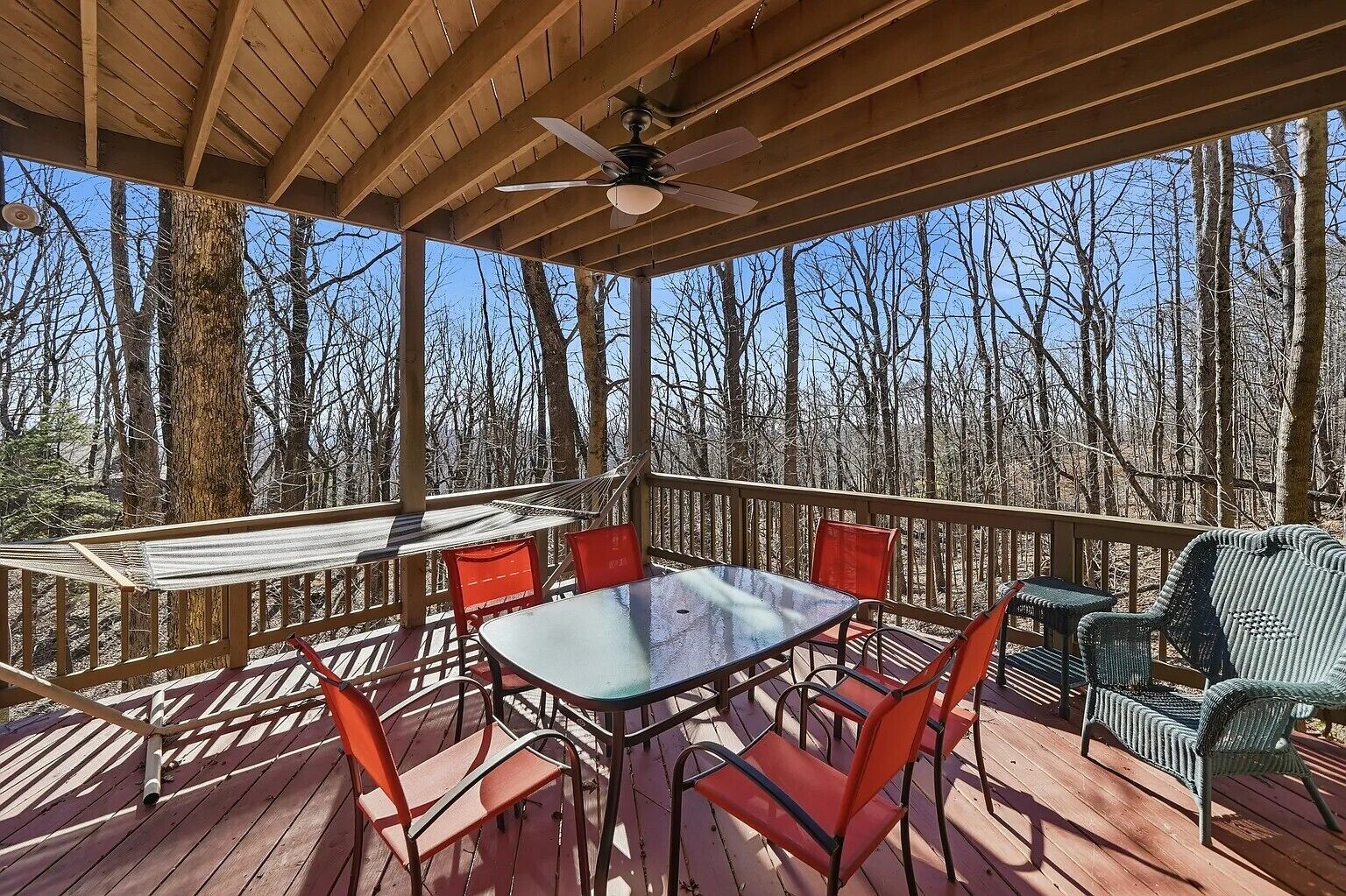 A covered outdoor deck with a table and chairs, surrounded by trees.