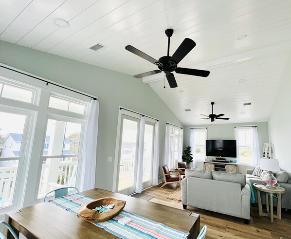 Uma sala de estar espaçosa com teto alto, janelas grandes e ventiladores no teto.