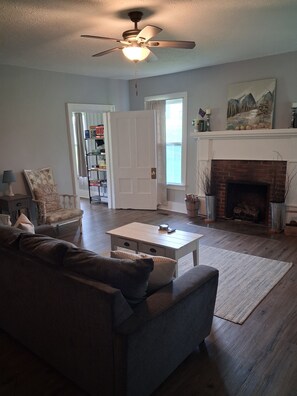 A living room with a sofa, coffee table, fireplace, and a ceiling fan. - Farmhouse with game room, creek and fire pit (Johnson City)