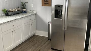 Une cuisine moderne avec des meubles blancs, un réfrigérateur en acier inoxydable, un distributeur d’eau et des éléments de décoration murale en bois.