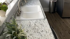 Eine Küche mit weißem Spülbecken, einer Arbeitsplatte aus Granit, Holzschränken und einem Edelstahl-Kühlschrank.