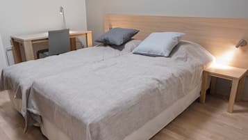 A neatly made bed with a grey blanket, two pillows, and a wooden headboard. There are two bedside tables with lamps, one on each side of the bed.