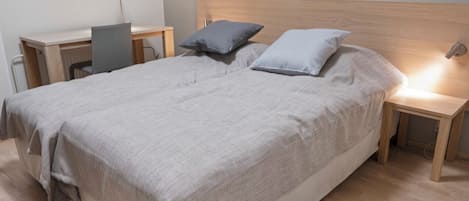 A neatly made bed with a grey blanket, two pillows, and a wooden headboard. There are two bedside tables with lamps, one on each side of the bed.