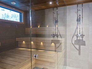 A modern shower area with glass doors, wooden benches, and a tiled wall. - Rukakylän helmi by Interhome (Kuusamo)