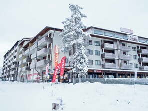 A multi-story hotel with balconies, ski rental signs, and a snow-covered tree in front. - Rukakylän helmi by Interhome (Kuusamo)
