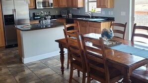 A modern kitchen with wooden cabinets, a stainless steel refrigerator, an island with seating, and a ceiling fan. - Classy 3-Bedroom Fishing Cottage with amazing lake and mountain views (Townsend)