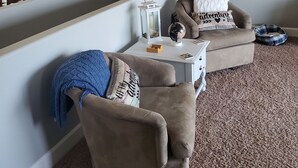 A cozy living room with two armchairs, a small table with a globe and a lantern, and a wall clock. - Classy 3-Bedroom Fishing Cottage with amazing lake and mountain views (Townsend)