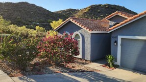 A residential house with a garage, surrounded by a landscaped garden with flowering plants and a view of a hilly landscape. - Desert Valley Stay - Mountain Views (Phoenix)