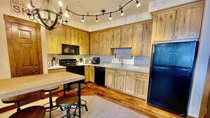 Une cuisine avec des meubles de rangement en bois, un réfrigérateur noir, un four à micro-ondes et un lustre.