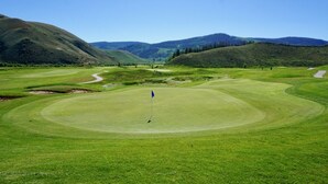 Un parcours de golf avec un mât de drapeau au centre, entouré de collines douces et sous un ciel dégagé.