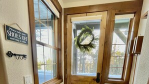 Une porte en bois ornée d’une guirlande, un panneau indiquant qu’il faut enlever ses chaussures, et un paillasson noir.