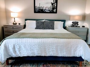 A neatly made bed with a patterned pillow, a headboard, and a framed picture on the wall.